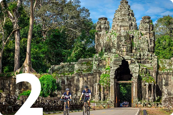 text:2; image: Bikers cycling in front of a stone statue