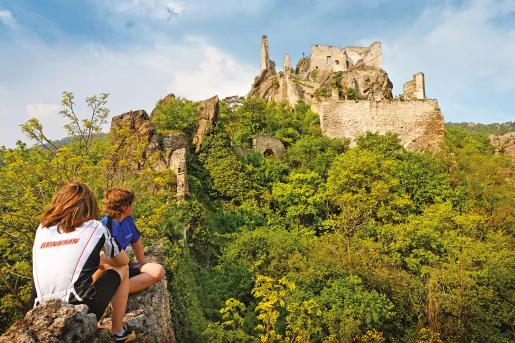 Two children sitting on a stone fence with building ruins in the background, Europe.
