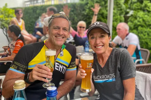 Two guests cheersing beer glasses, smiling at camera.