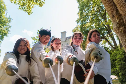 Five young guests in fencing gear, pointing sabers at camera.