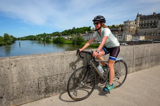 Guest cycling over concrete bridge, river, riverside town behind her.
