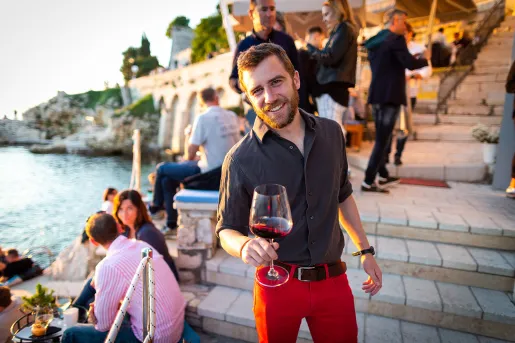 Man among group of other people, wine glass in hand, sunset.