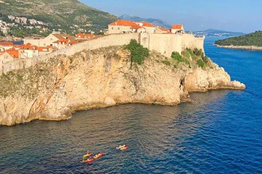 Wide shot of walled cliffside houses, guests kayaking below.