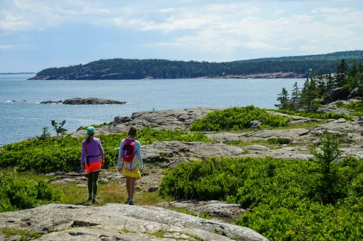 Two guests hiking along a lakeshore, forest landscape and lake itself in background.