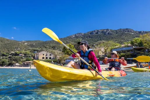 Two guests beginning to kayak on blue water, beach houses in background.