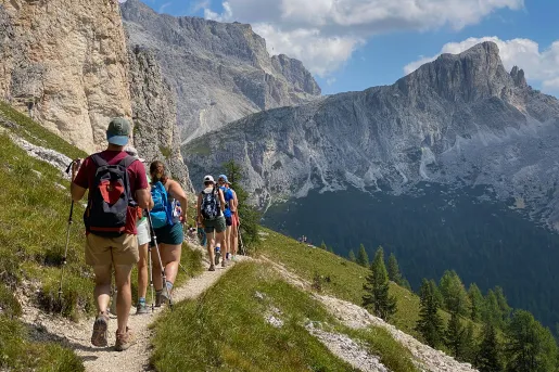 Group of guests walking along hillside trail, cliffs to left, sprawling mountains to right.