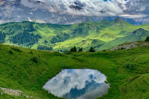 Wide shot of green, hilly, mountainous vista, small pool in foreground.