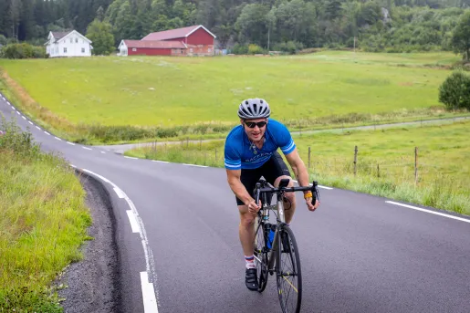 Man riding bike on asphalt road through a grassy field