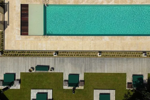 Sky view of an outdoor pool with green pool chairs and grass areas surrounding the pool