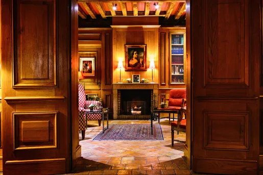Library with large wooden doors, and a painting of a woman above a stone fireplace