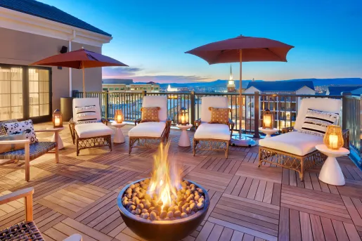 Wooden balcony with white chairs surrounding a stone firepit
