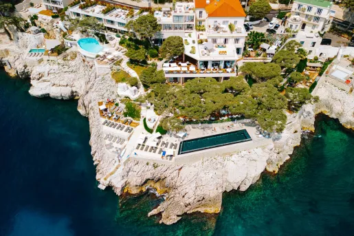 Sky view of a hotel complex with an outdoor pool on a cliff, next to the ocean