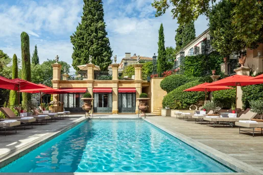Outdoor pool with a yellow building in the background, with red umbrellas surrounding the pool
