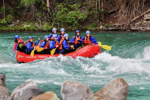 Group of men and women in a red raft paddling through a river
