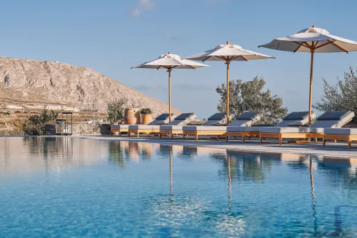 Outdoor pool surrounded by chairs and umbrellas, with a mountain in the background