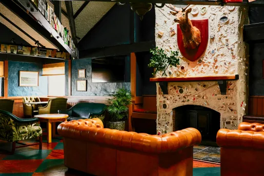 Indoor lounge area with orange and green couches surrounding a stone fireplace