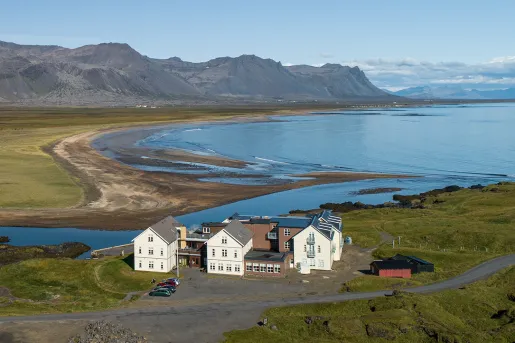 Exterior, sky view of a white and brown hotel building, with a large lake and mountain in the background