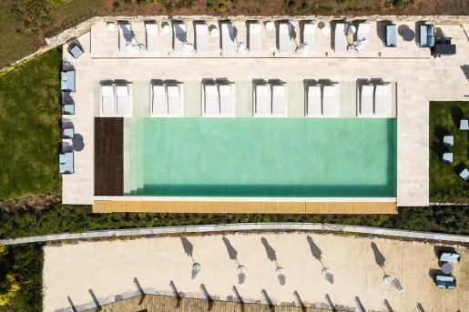 Sky view of outdoor pool surrounded by reclining chairs on a stone walkway