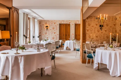Indoor dining area with flower wallpaper, white dining tables, and two candles on each table