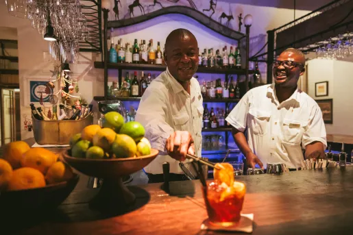 Two bartenders making alcoholic drinks and adding an orange slice to one drink