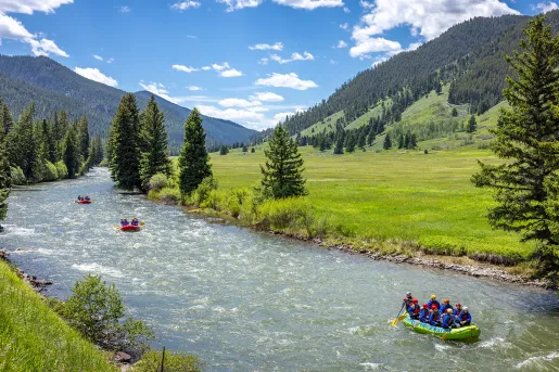 River in between two grassy valleys, with three rafts full of people