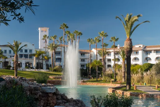 External view of a white hotel building with a large pond and a fountain in front