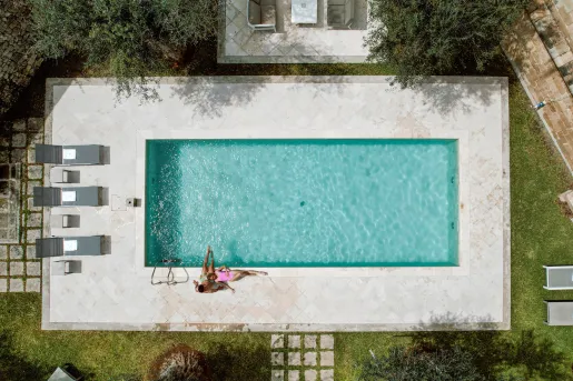 Man and woman laying down in an outdoor pool with gray pool chairs on the left