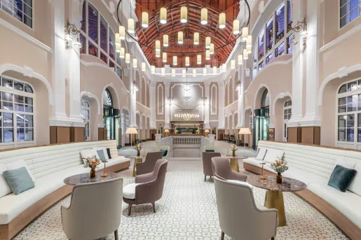 Large, wide hall with white and tan cushioned chairs and a large, circular light fixture in the center