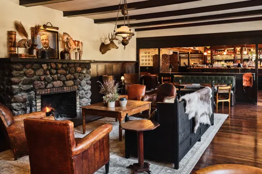 Lobby with leather couches in front of a fire place, with a bar in the back right
