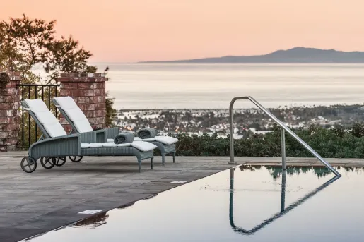 Outdoor pool with two pool chairs, overlooking a town and the ocean