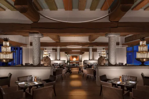 Dimly lit dining area with giant stone pillars and leather chairs around each table