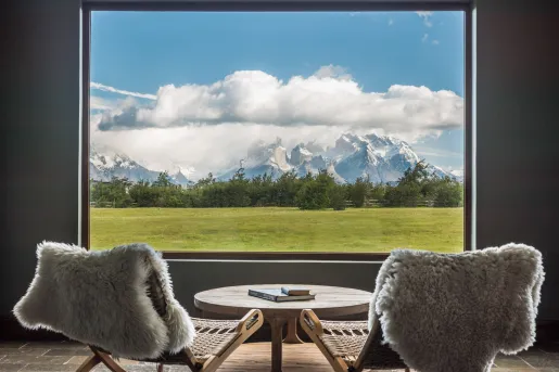 Two woven chairs with fur on them, facing a window looking out to snow capped mountains
