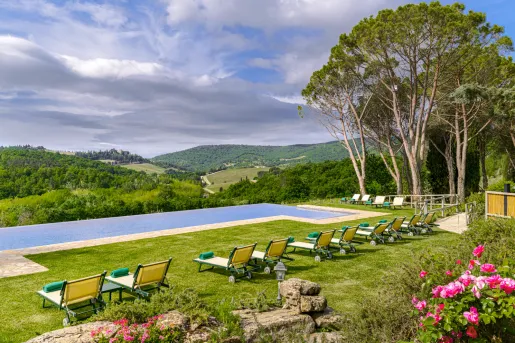 Outdoor infinity pool surrounded by green and red reclining chairs with a view of mountains in the distance