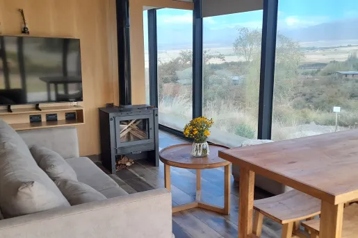 Couche with a wooden table and metal fireplace, looking out towards a glass wall with a valley outside