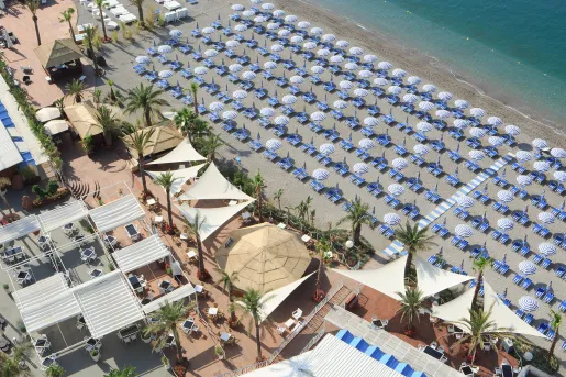 Sky view of a beach with white and blue chairs and umbrellas lined up on the sand