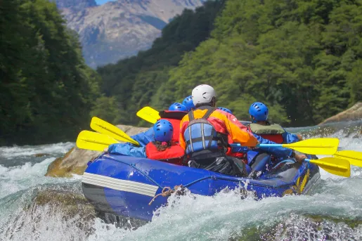 Group of people on a blue raft, paddling through an active river