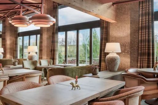 Lounge and seating area with wooden table and cushioned chairs, with large windows in the back