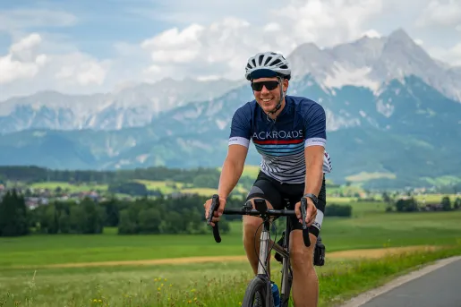 Man riding a bike on an empty road, with a large field and tall mountains in the background