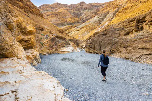 Woman walking a rocky trail in between two orange canyons