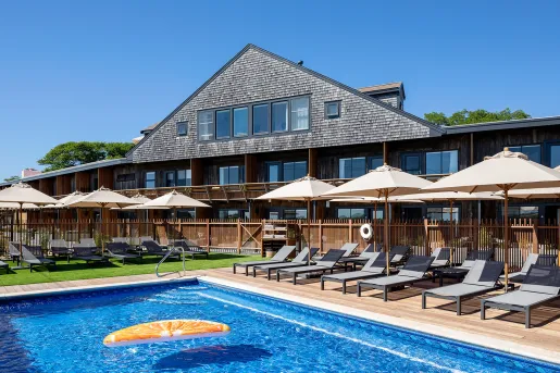 Outdoor pool surrounded by gray chairs and white umbrellas, with a building in the background