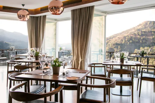Restaurant with wooden dining tables and chairs, with large open doors in the background