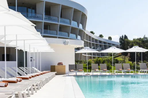 Outdoor pool, with white umbrellas and chairs surrounding the pool and a building in the background