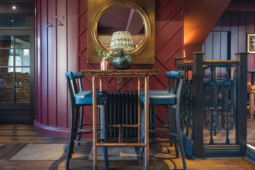Dining table with a copper tables and blue stools, with a large mirror hanging on the wall