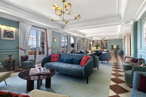 Long room with blue, cushioned sofas with large doors leading to a patio