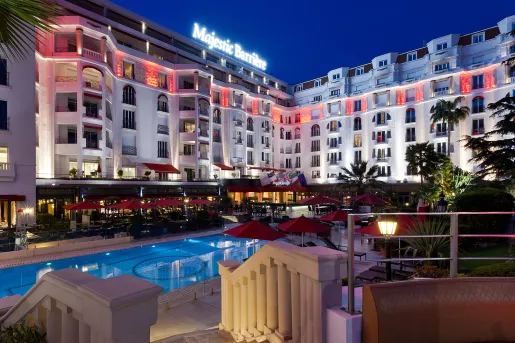 Exterior view of hotel building with an outdoor pool and red umbrellas