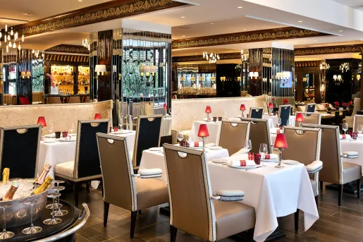 Indoor dining hall with multiple dining tables and cushioned chairs, with wine glasses on each table