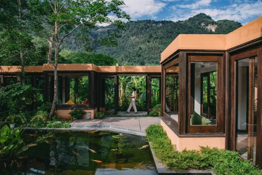 Exterior view of wooden building with large glass windows and a pond in front