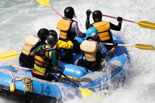 Group of people paddling on a blue raft in the middle of a river