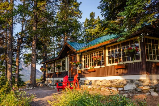 Exterior view of cabin building with two red chairs in front and large trees in the background