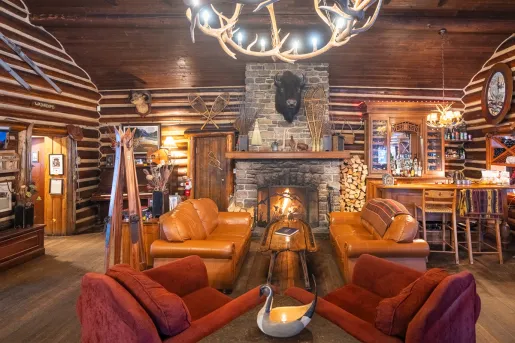 Room in a cabin with leather chairs and a stone fireplace in the center